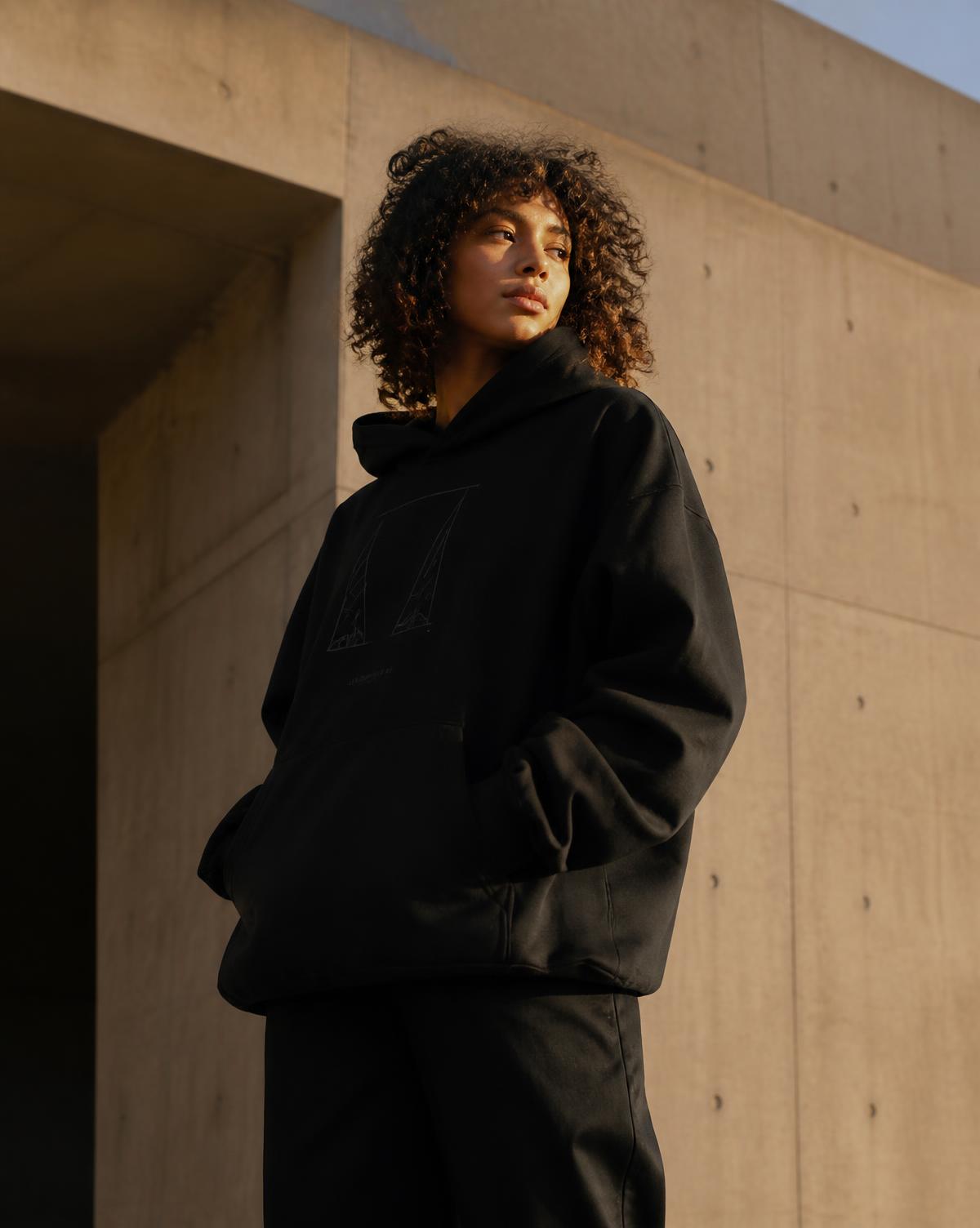 Woman wearing an oversized black hoodie in front of modern concrete architecture